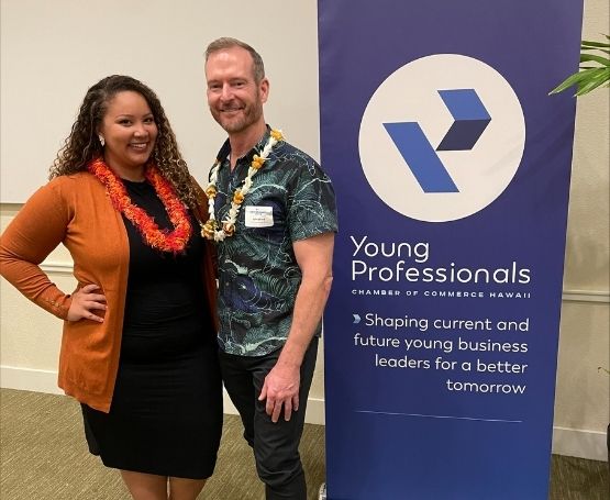 A man and woman posing next to a Young Professionals event pull-up banner.